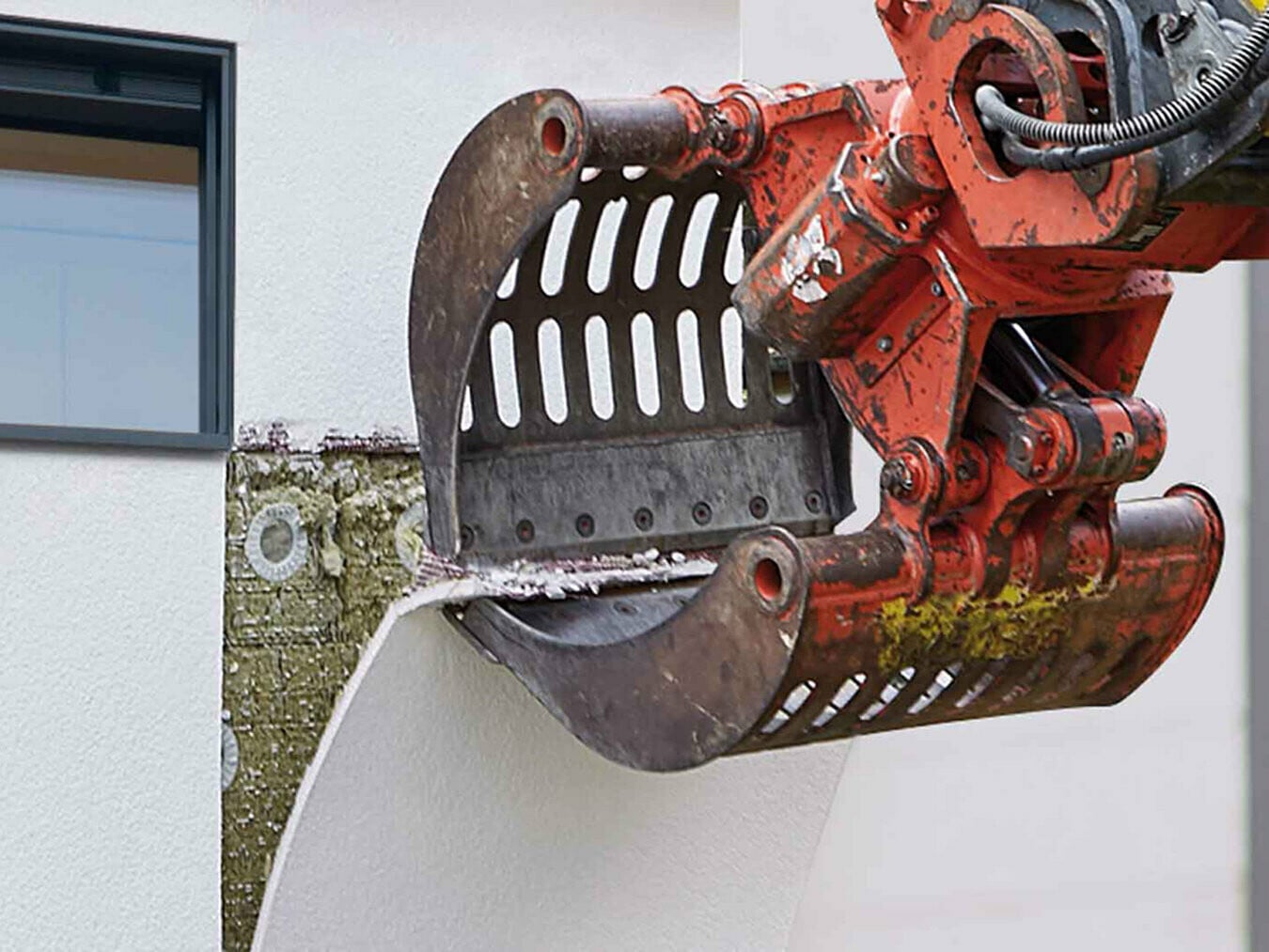 Eine Baggerschaufel zieht die in kleine Felder unterteilte Putzschicht samt Separationsgewebe sauber von der Mineralwolle ab. 