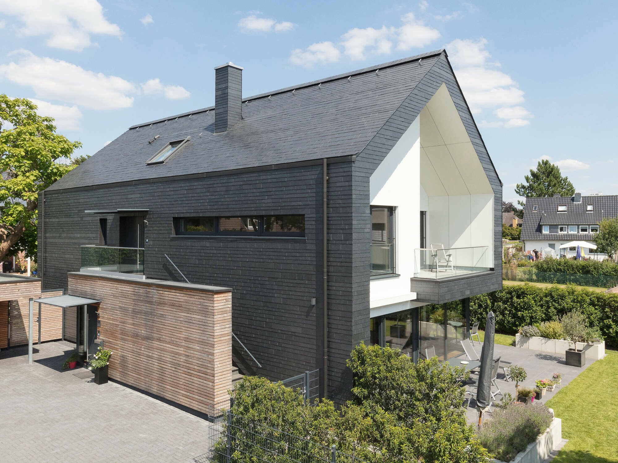 Dunkle Hülle, weiße Ausschnitte des Gebäudekörpers: Das Wohnhaus in Kaarst erhält mit Schiefer an Dach und Fassade eine monolithische Wirkung.