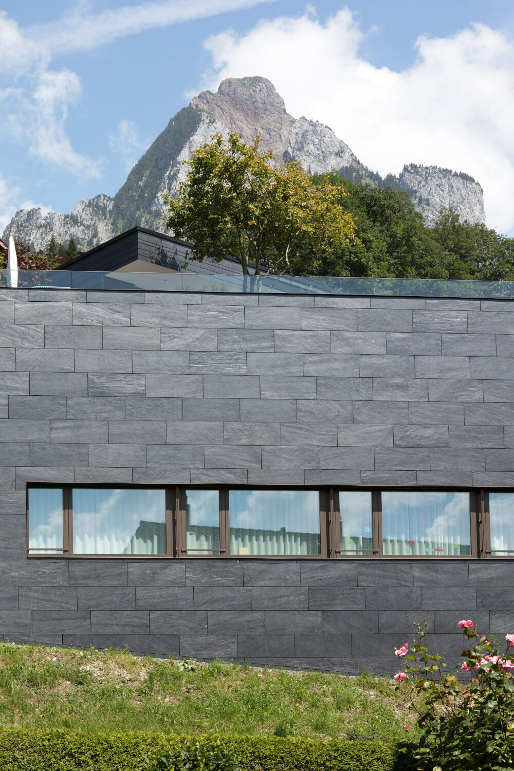 Der untere, kleinere Baukörper ist mit großformatigen Schieferplatten bekleidet. Rückwärtig und nicht sichtbar befestigt, erzeugen sie eine ruhige Wirkung, eher wie Mauerwerk.
