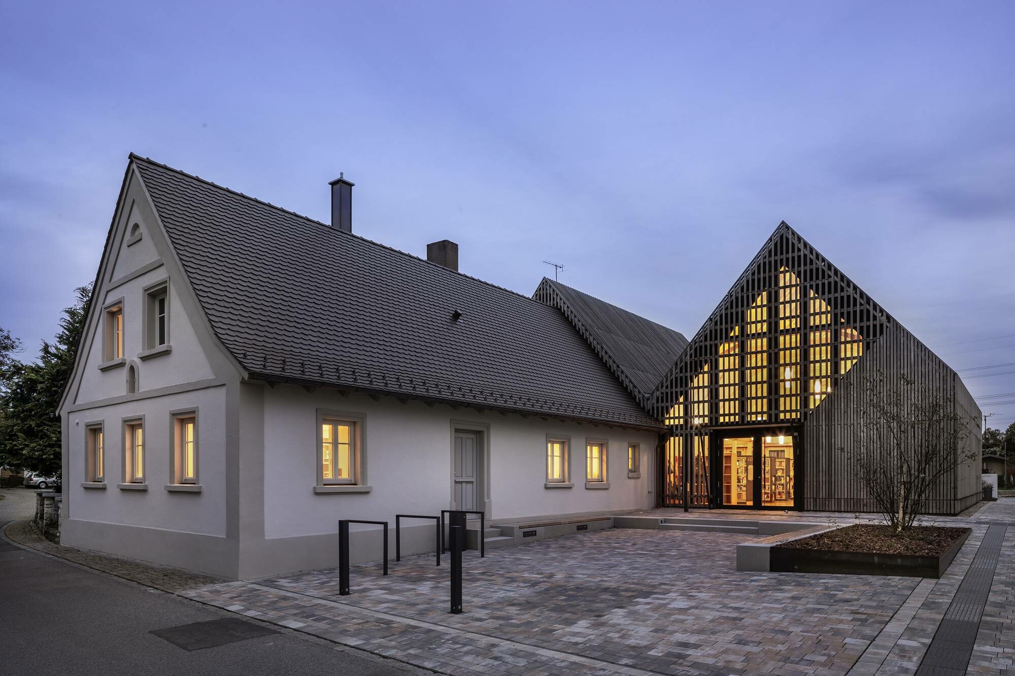 Von der Straßenseite betrachtet stülpt sich der neue Anbau buchstäblich über das historische, deutlich kleinere Stallgebäude.