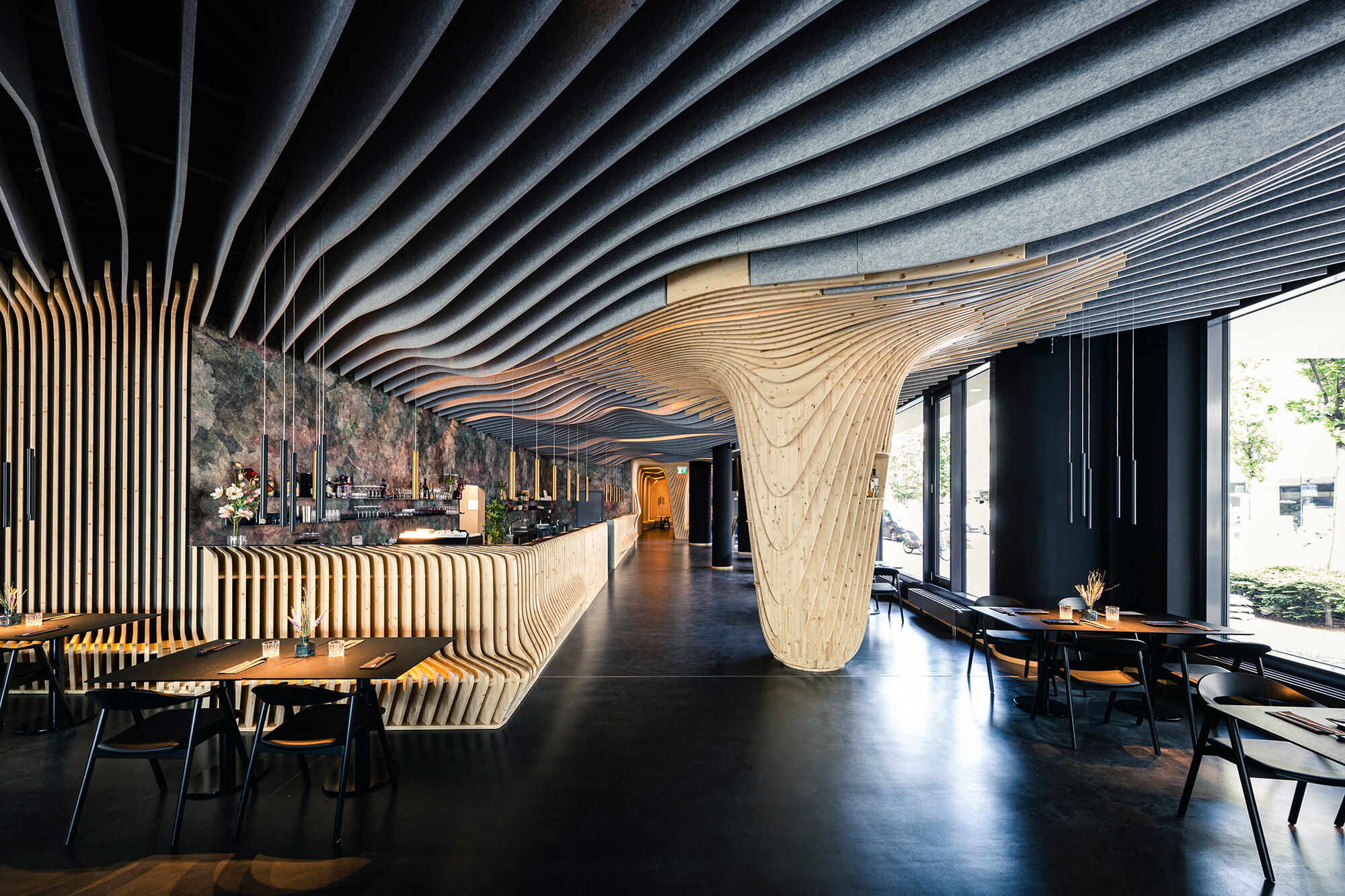 Die Lamellen umspielen wellenförmig die Raumgrenzen und ziehen sich von der Decke über die Wände bis zum Boden des Restaurants.