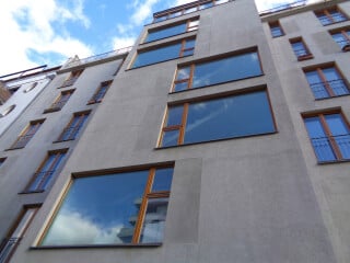 Festverglaste Fenster haben die gleichen bauphysikalischen Eigenschaften wie Fenster mit Öffnungsflügeln. Im Bild: festverglaste bodentiefe Fenster mit grau verputzten Belüftungsklappen, die als anleiterbare Rettungsöffnungen dienen (Block + Void House, Bundschuh Architekten, 2016).