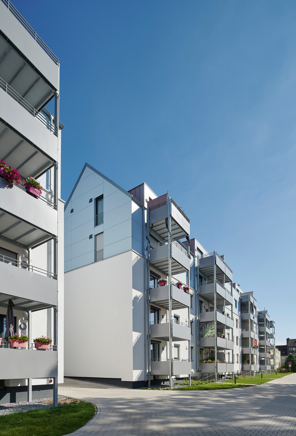 Das Bestandsmauerwerk wurde weiß verputzt, die Aufstockung mit einer vorgehängten, hinterlüfteten Fassade aus hellblauen rechteckigen Paneelen verkleidet.