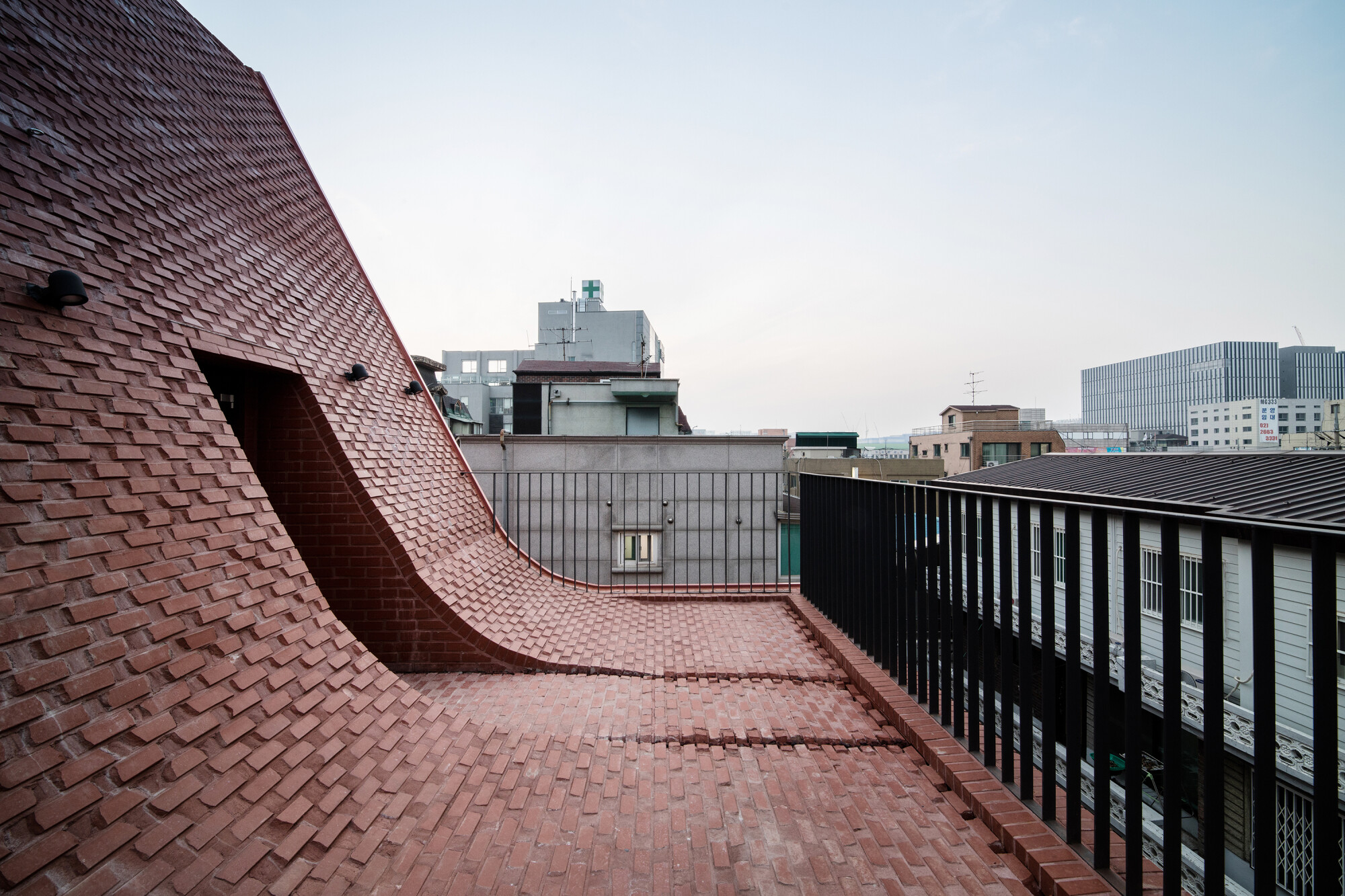 Das an der Nordseite steil geneigte Dach geht mit einer Rundung in eine Dachterrasse oberhalb des zweiten Stockwerks über. 