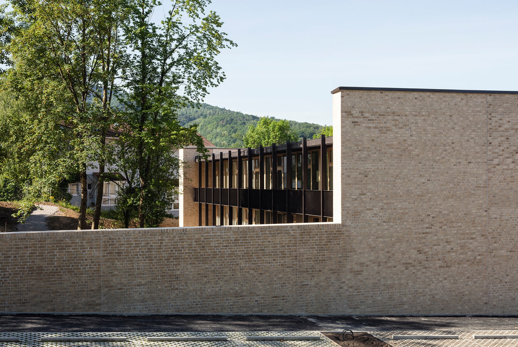 Zur Straße und zu den seitlichen Nachbarn zeigt sich das zweigeschossige Gebäude zurückhaltend bis verschlossen und von einer niedrigen Mauer umgeben.