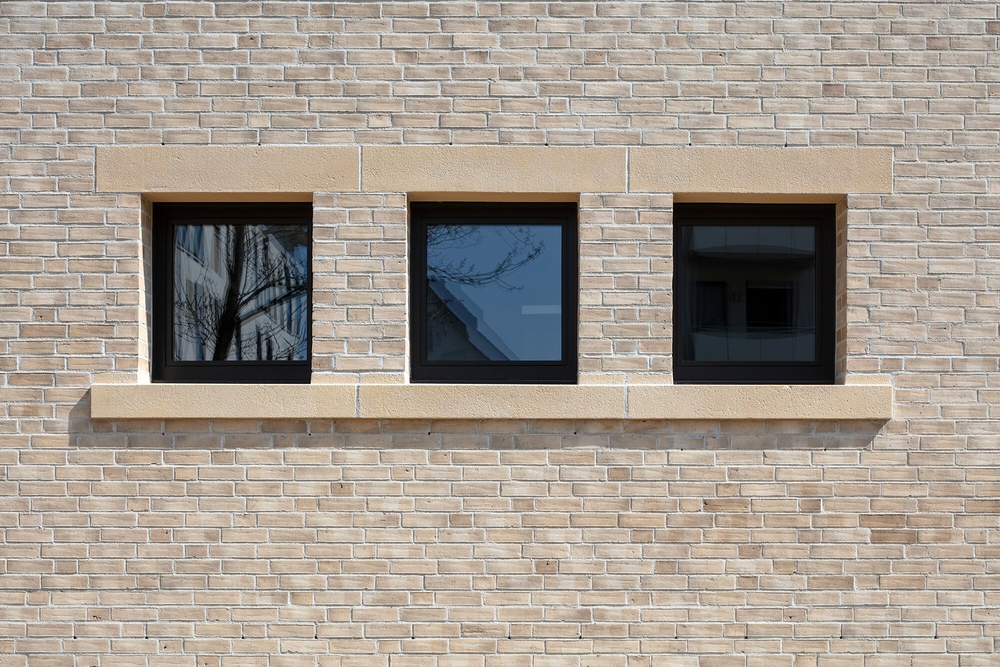 Eine helle sandsteinfarbene Klinkerwand mit nur wenigen, aber sorgfältig platzierten Fensteröffnungen bildet eine Art schützende Schale um ein kompaktes Volumen.