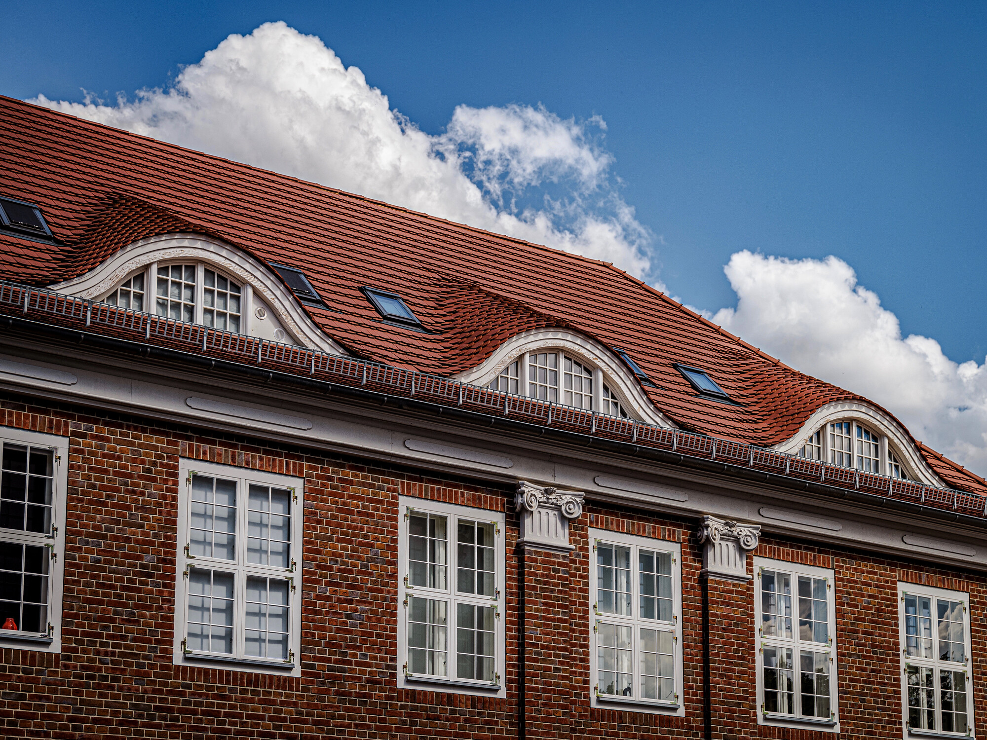 Mehrere gleichförmige Feledermausfenster neben kleinen Dachluken.