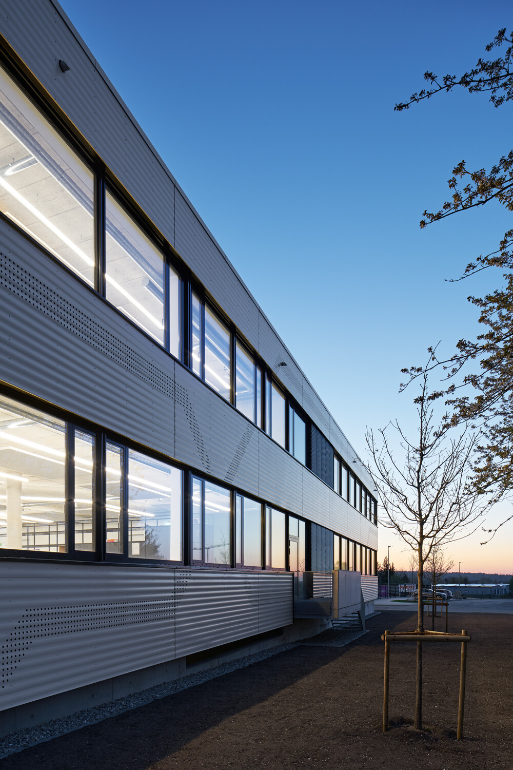 Eine weiße, hinterlüftete Metallfassade und Fensterbänder prägen die Fassade.