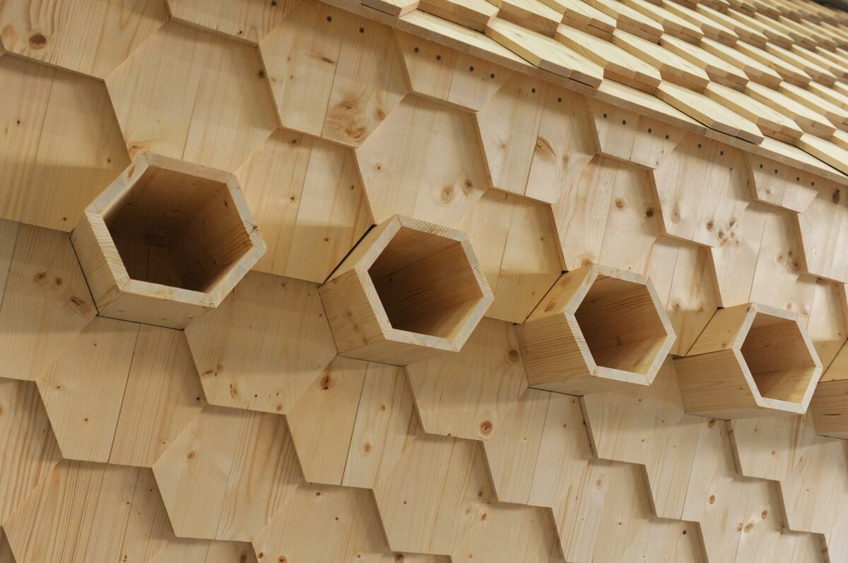 Über acht seitlich angeordnete sechseckige Ausgangsrohre aus Holz können die Bienen hinein- und hinausfliegen.