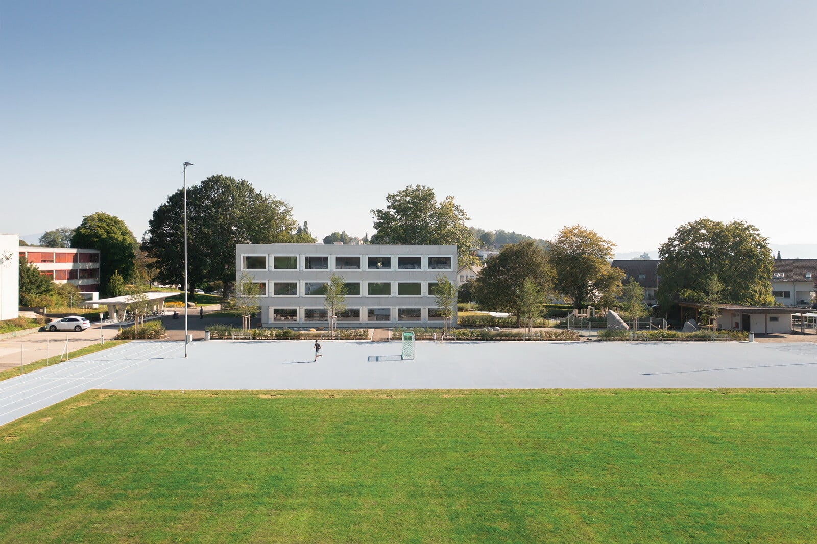 Über Jahrzehnte entstanden um einen zentralen Sportplatz herum verschiedene, architektonisch schlichte Bauten, die nun an der Nordost-Ecke um den dreigeschossigen Neubau mit Klassenzimmern und einem Kindergarten ergänzt wurden.