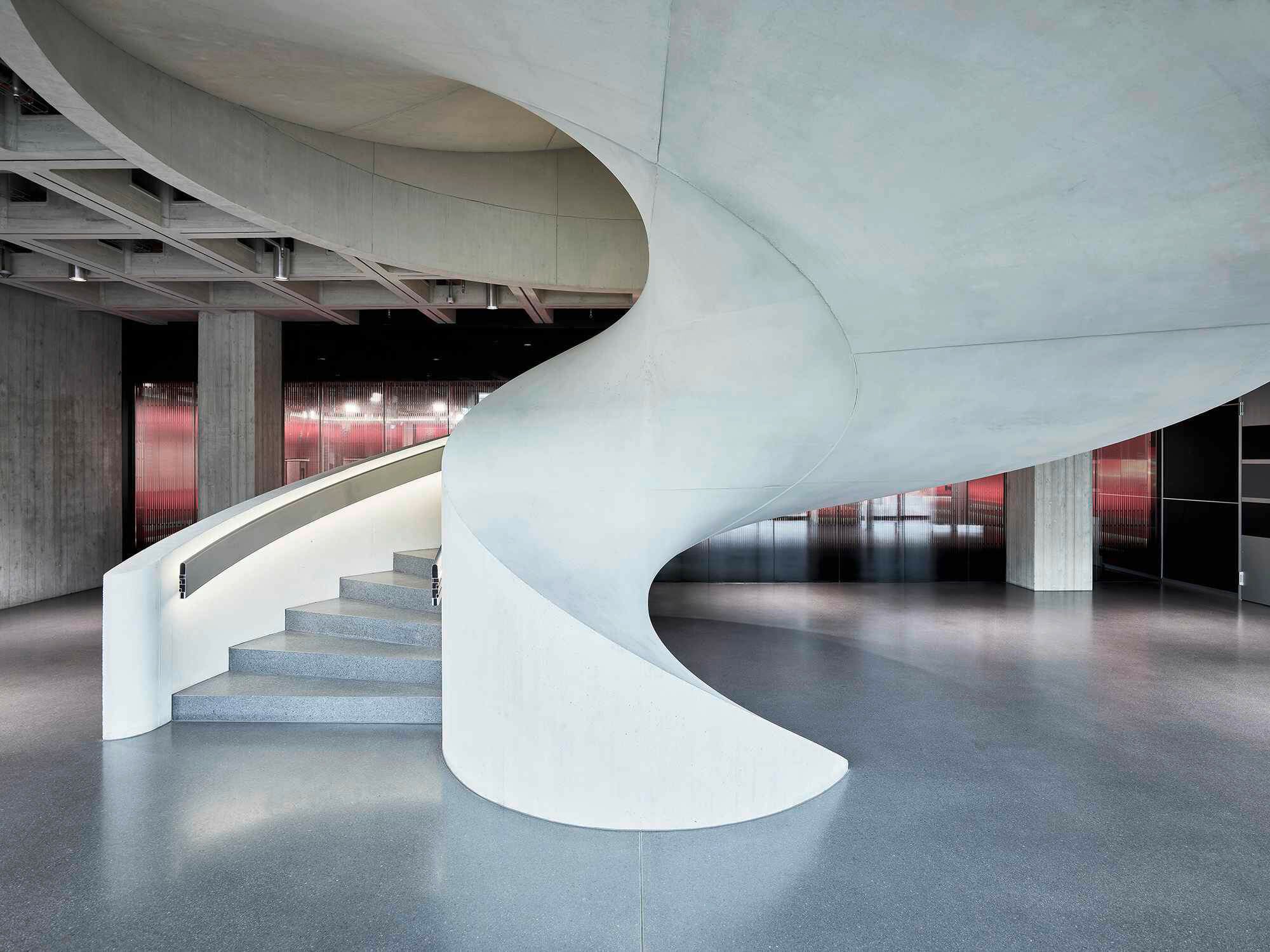 Die Treppe im Foyer erscheint aufgrund der schrägen Untersichten und der spiralartigen Geometrie des Treppenauges als Wirbel.