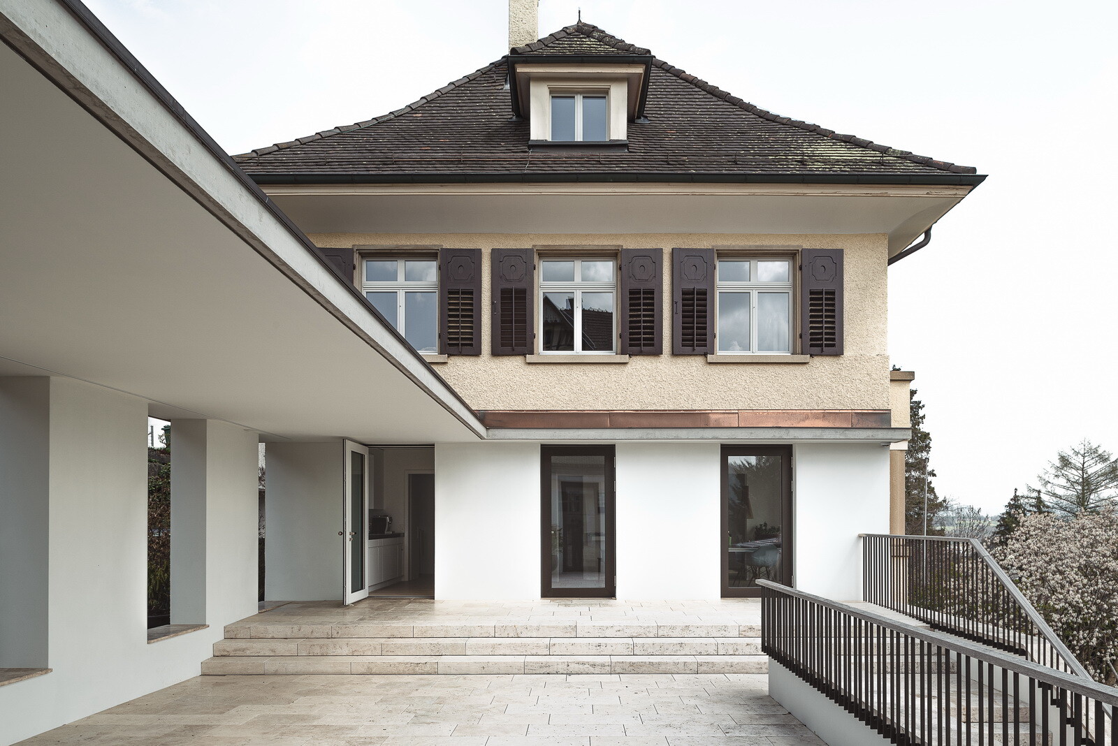 Eine Mauer zur nördlichen Grundstücksgrenze verbindet Alt- und Neubau miteinander, sodass der Außenbereich an drei Seiten gefasst wird.