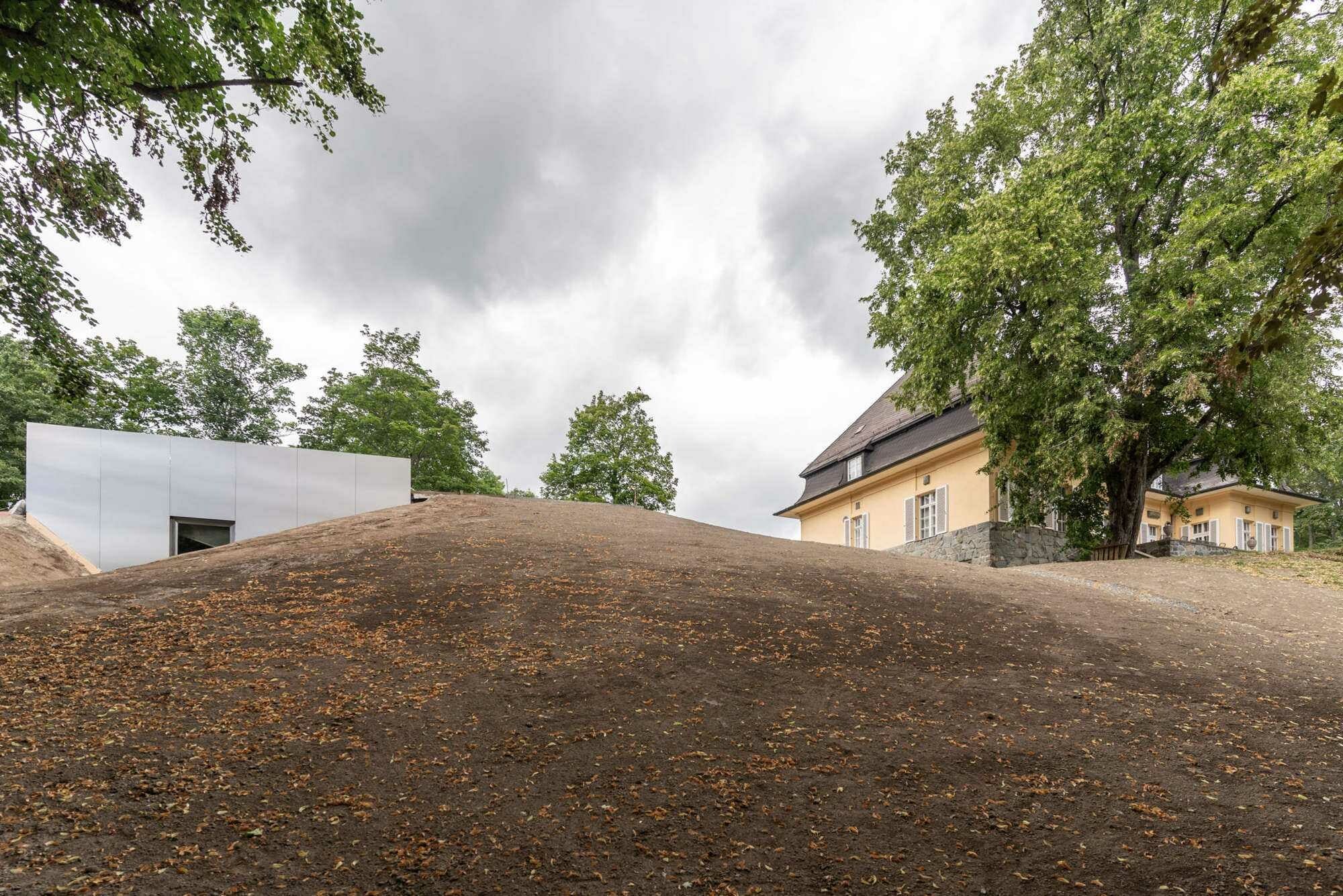 Lediglich zwei schmale Edelstahlfassaden am südlichen Hang deuten an, dass sich unter der Erde neue Architektur befindet.