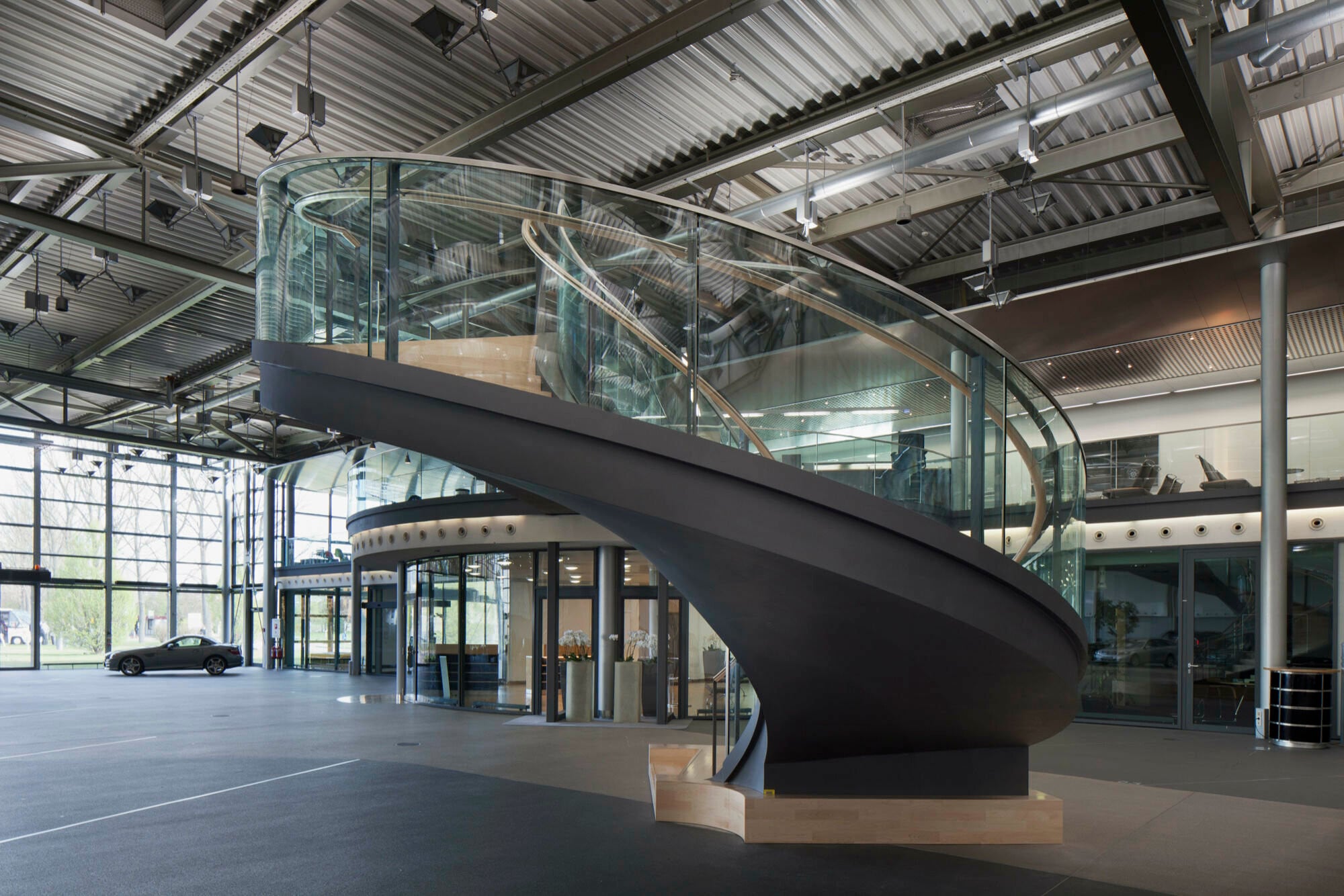 Gleichmäßig gerundete Wendeltreppe aus Stahl mit ebenfalls gerundeter Glasbrüstung im Foyer des Kundenzentrums bei Mercedes Benz im Werk Stuttgart/Sindelfingen.