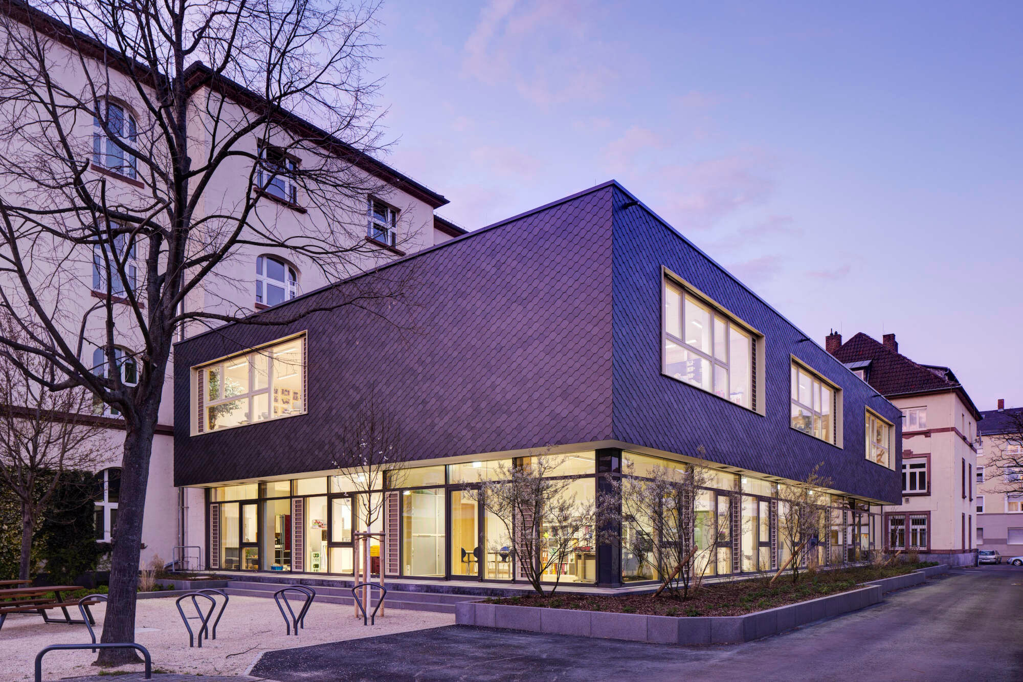 Deutlich hebt sich der Neubau ab. Mit Innenbeleuchtung wirkt das verglaste Erdgeschoss sehr einladend.