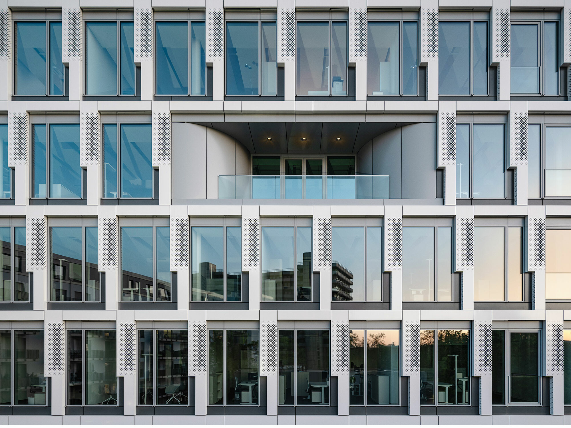 Opake und transparente Flächen wechseln sich an der Fassade ab, während die Vertikalpaneele vor den Lüftungselementen perforiert sind. 