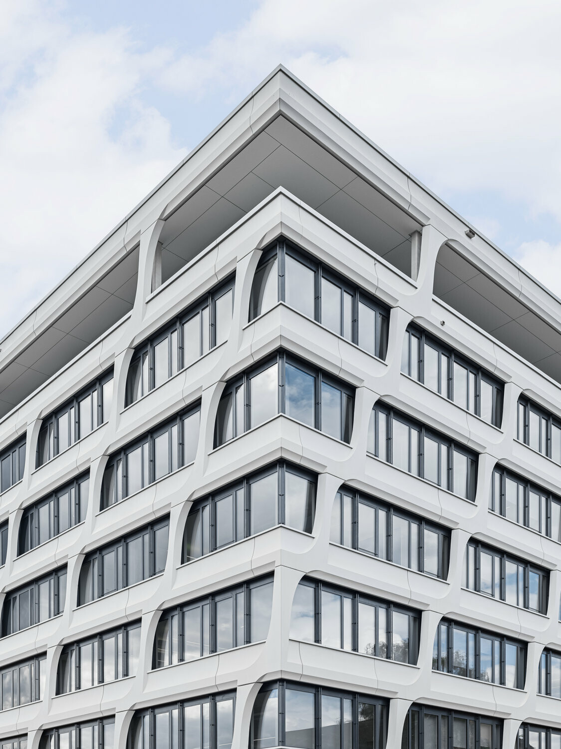 Weiße, geschwungene Fassadenelemente aus Sichtbeton prägen die Fassade des Ensembles.