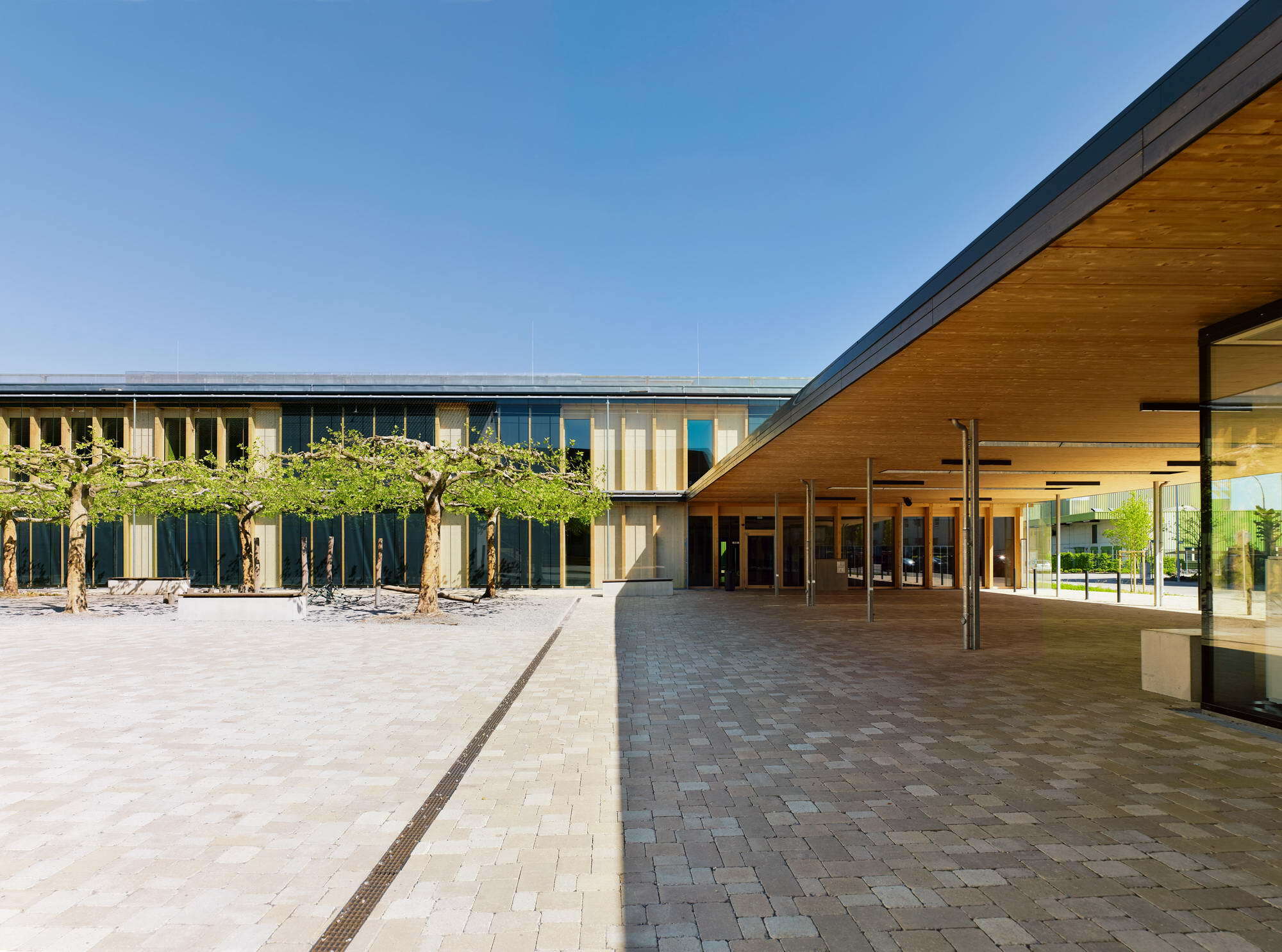 Eine Pergola verbindet Klassenzimmertrakt und Mensabau miteinander, wodurch der Schulhof gefasst wird.