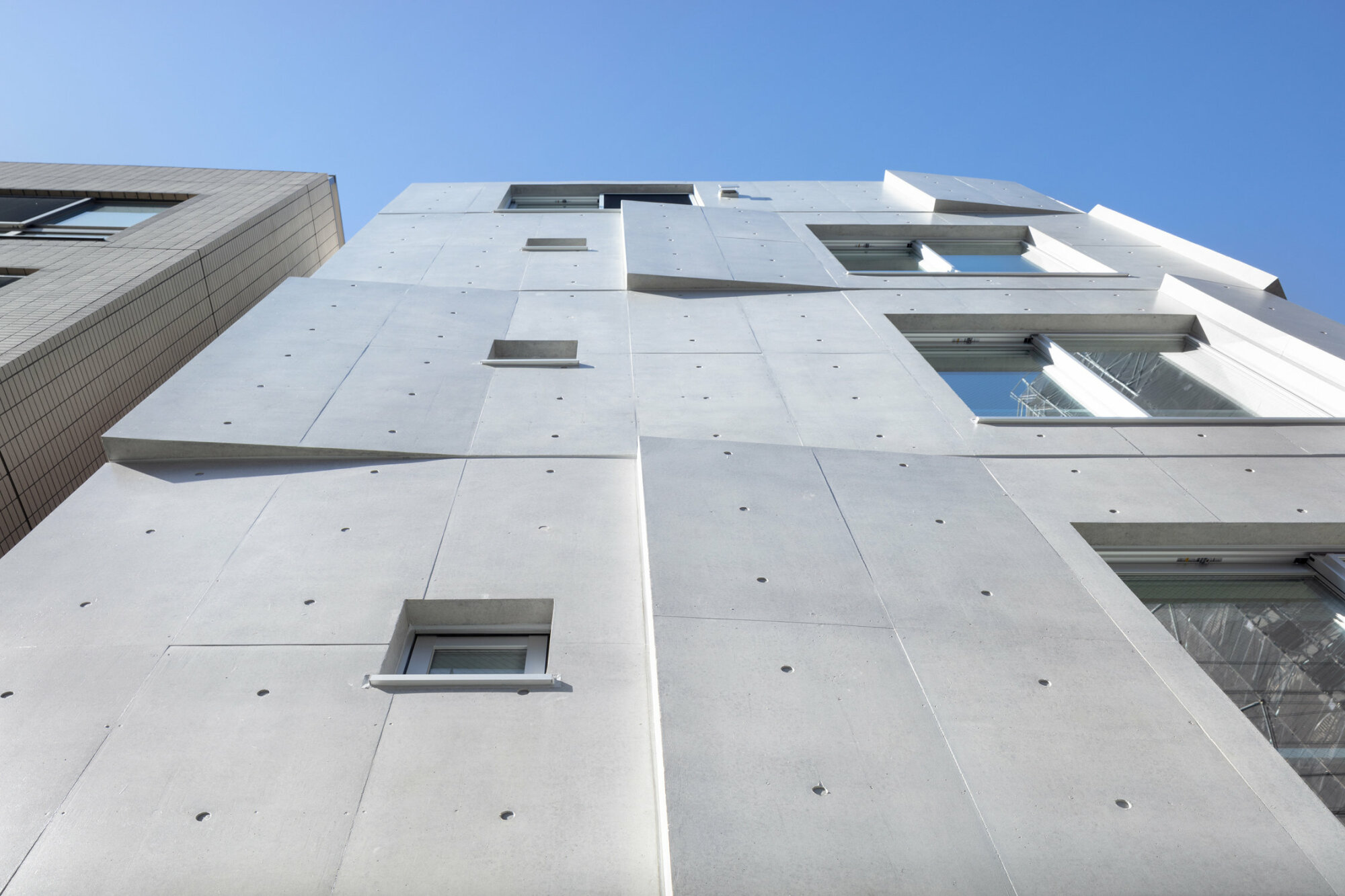 Neben den zahlreichen Ankerlöchern der Trägerwandschalung prägen die Fassade die Kreuzfugen der Schaltafeln sowie kleine, punktförmige Vertiefungen, die anzeigen, wo die Schalhaut mit Nägeln auf den Trägerelementen befestigt wurde. 