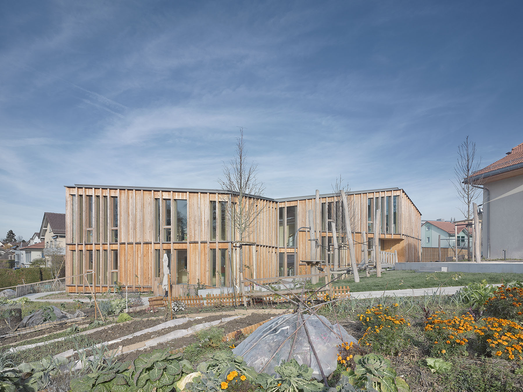 Die Kindertagesstätte nach Plänen von Atelier Pulver Architectes aus südwestlicher Richtung mit angrenzenden Kleingärten
