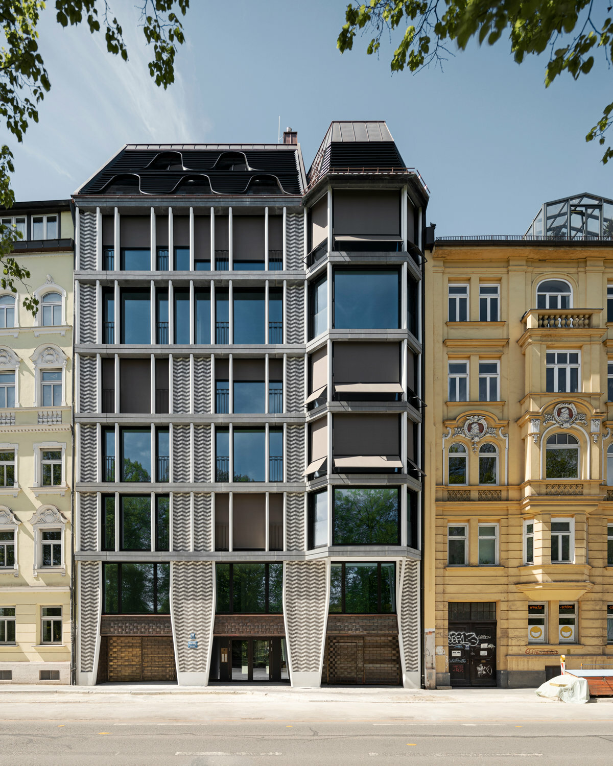Grundlegende gestalterische Elemente der Hülle sind horizontale Gesimsbänder und schlanke, paarweise angeordnete Säulen aus Beton sowie raffiniert im Zickzack-Muster verputzte Wandflächen. 
