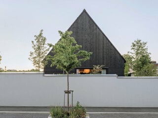 Im Süden ist das Grundstück durch eine Mauer begrenzt. Bernado Bader Architekten planten das schlichte schwarze Einfamilienhaus mit Satteldach.