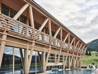Der neue Wellnessbereich ist ein Holzbau mit weitem Dachüberstand und umlaufenden Fluchtbalkonen. Markante Schräg- und Diagonalstützen prägen das Gebäude, das sich allseitig mit großen Verglasungen öffnet.