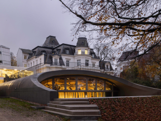 Zwischen bestehenden Budge-Palais, Sitz der Hochschule für Musik und Theater HfMT in Hamburg, und Ufer der Außenalster lugt die neue JazzHall aus der Wiese hervor.