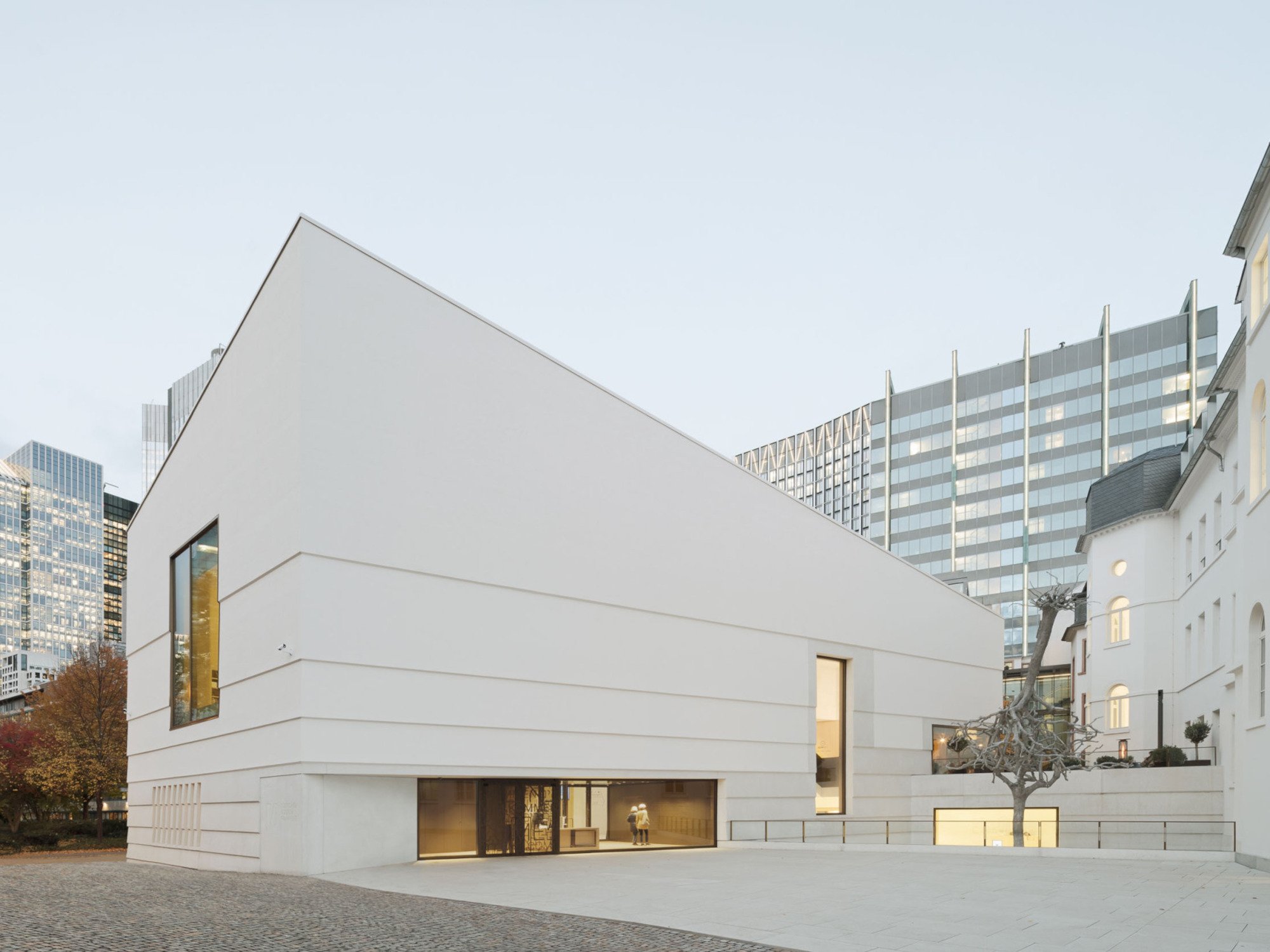 Zwischen Neu und Alt entstand ein öffentlicher Platz: Staab Architekten schufen einen monolithisch wirkenden Baukörper, der die Farbgebung des Bestands aufnimmt und dessen strukturierte Putzfassade auf die horizontale Gliederung seines Gegenübers verweist.