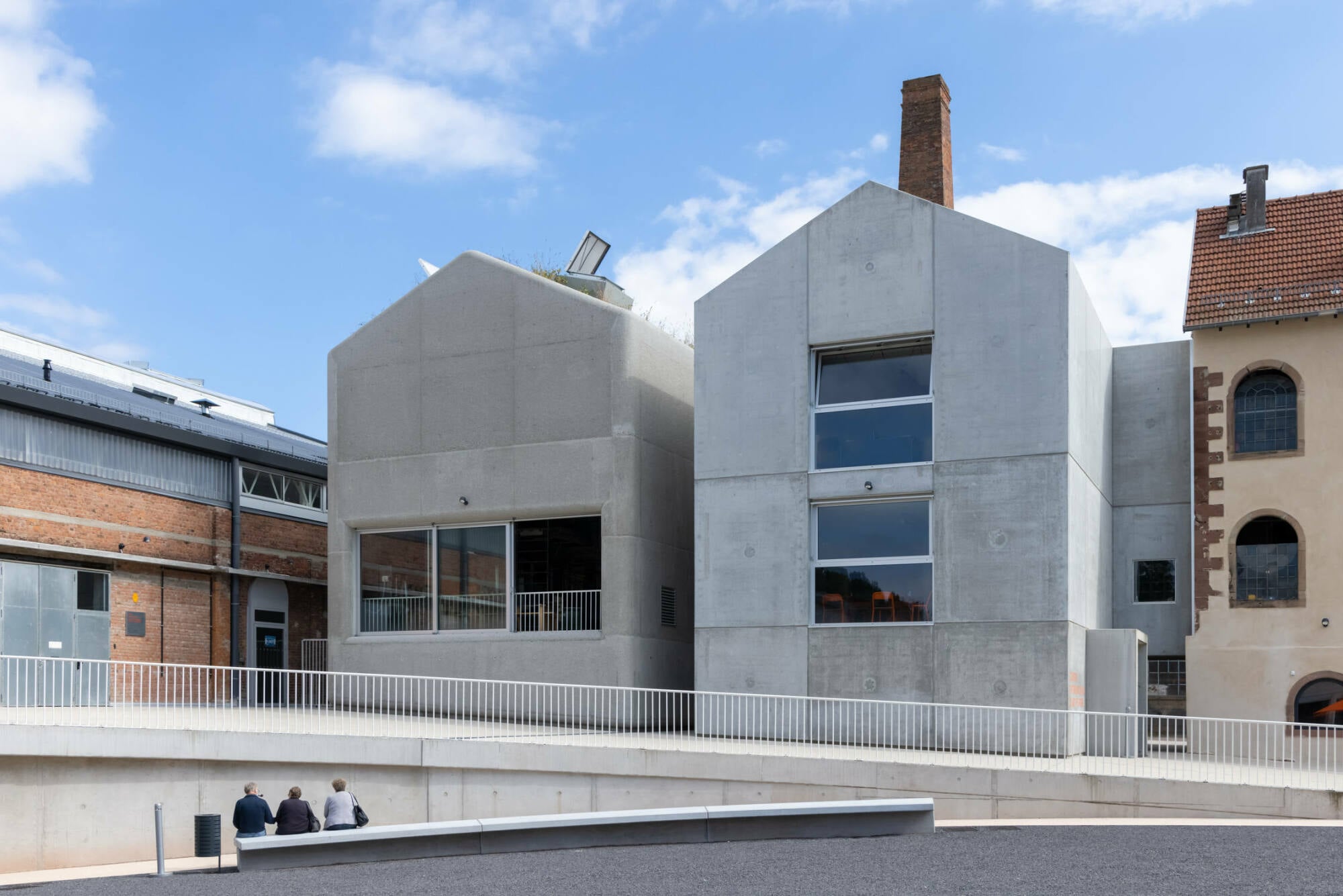 Während der eine Bau in Ortbeton ausgeführt wurde und gestockte Oberflächen zeigt, prägen den anderen glatte Fertigteilelemente.