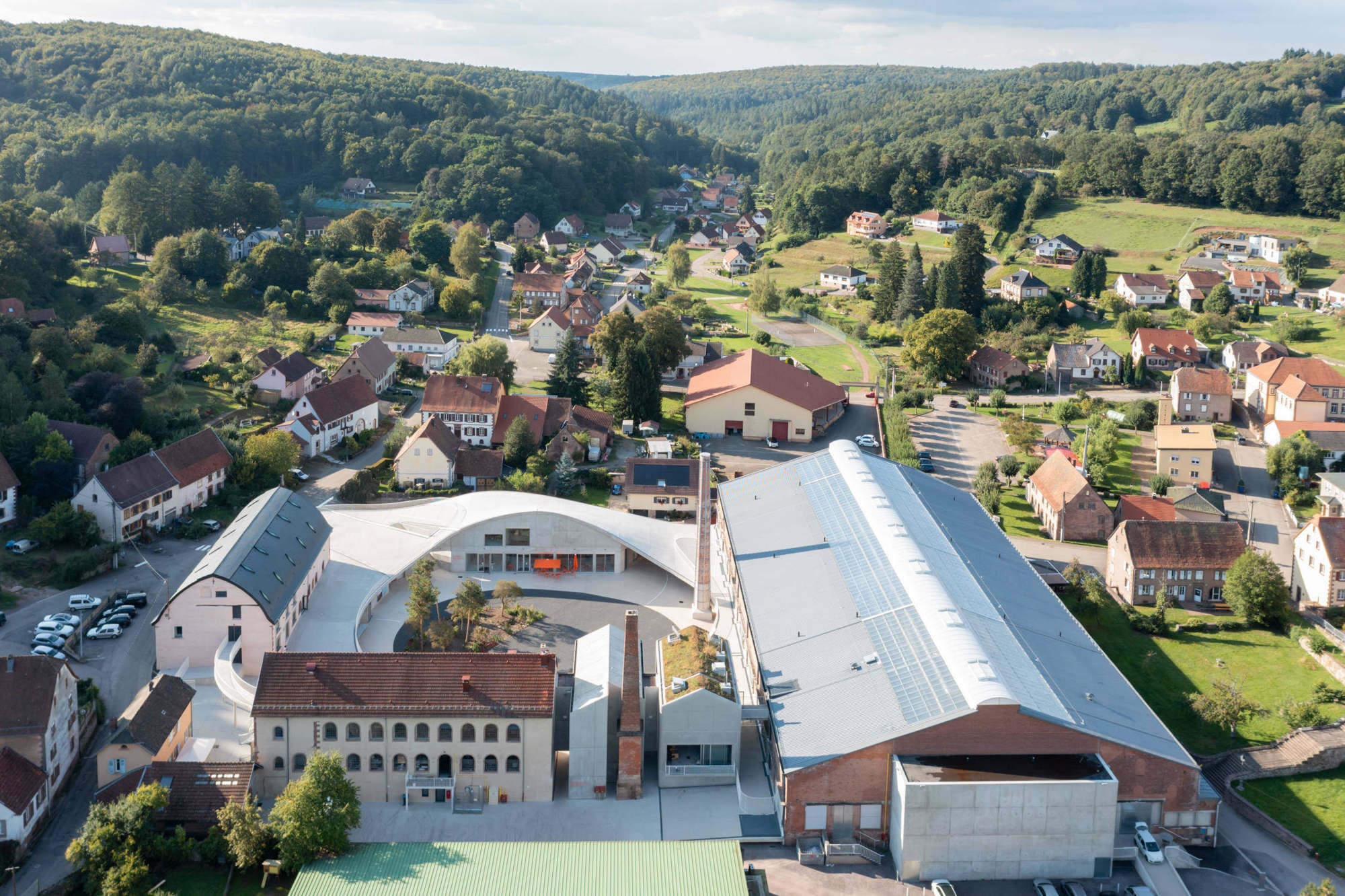 Ein wellenartiges Dach aus Beton fasst nun ein im Grundriss blasenförmiges Rund und verbindet die unterschiedlichen Nutzungen.