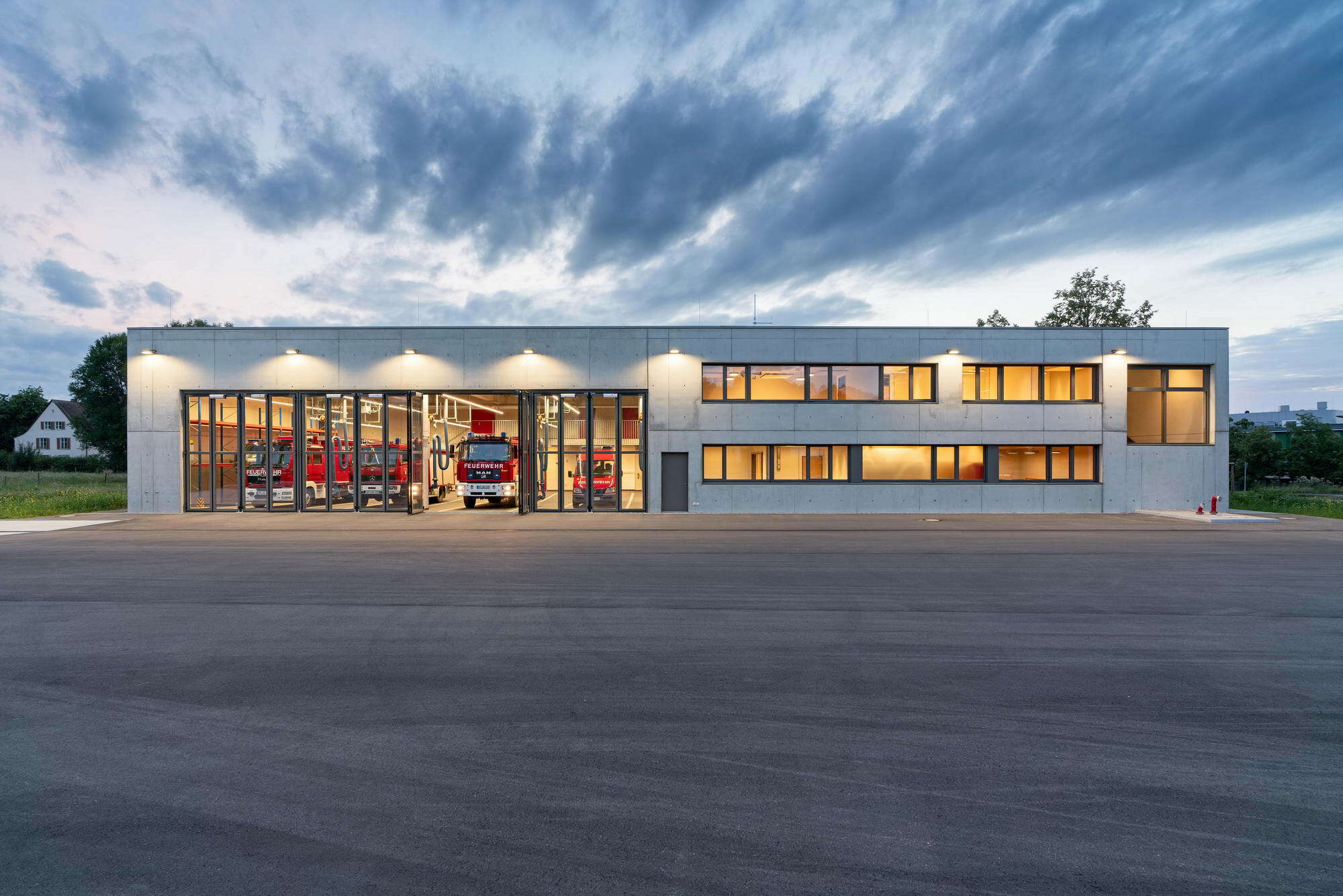 Der Neubau, so der Wunsch der Nutzerin, sollte zwei lange Seiten haben, sodass die Feuerwehrleute bei einem Notfall an der einen Seite mit ihren privaten Autos ankommen und auf der anderen Seite mit den Einsatzfahrzeugen ausfahren können, ohne sich dabei gegenseitig zu behindern. 
