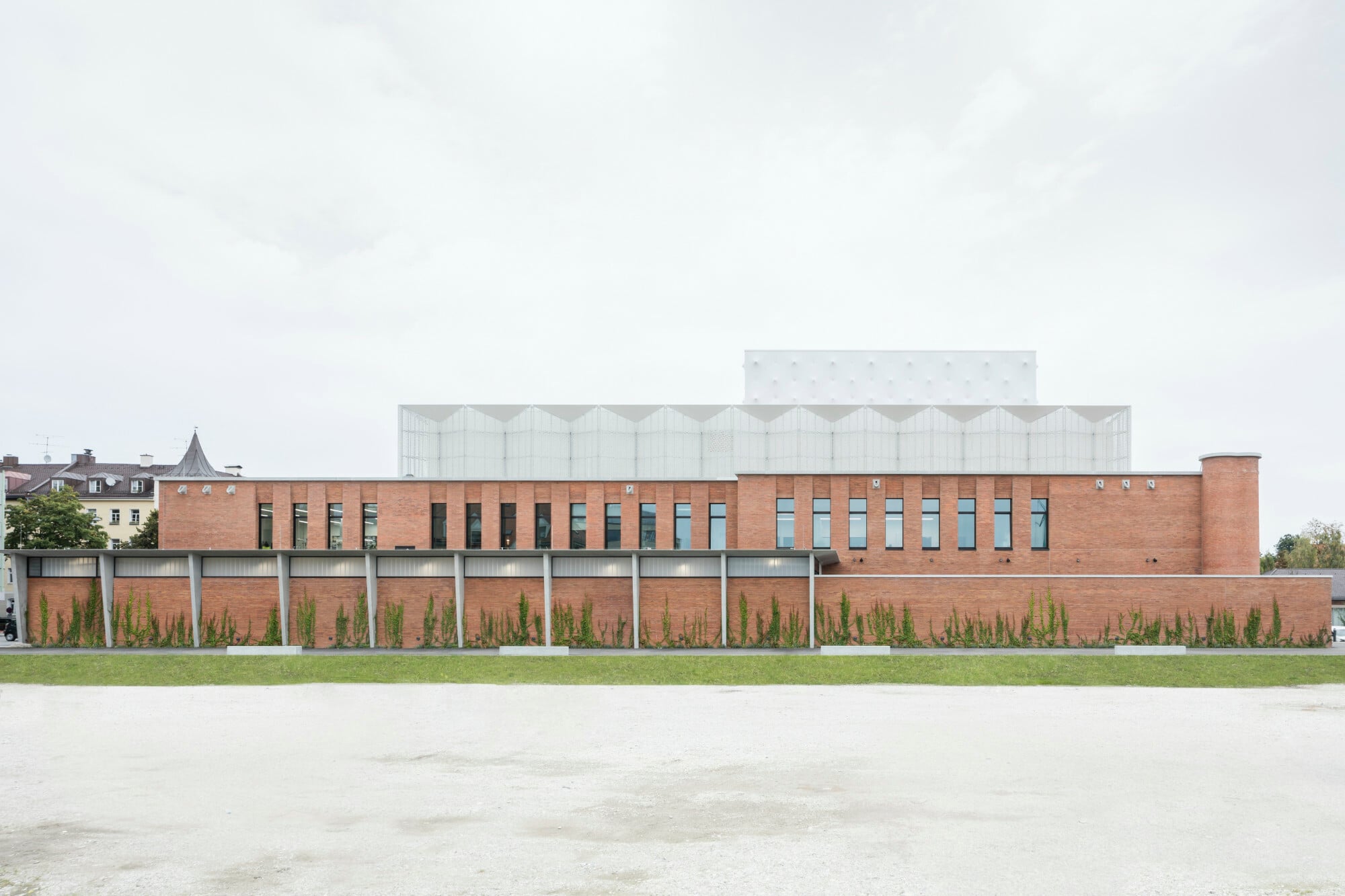 Die gestaffelten Funktionsbereiche zeigen jeweils unterschiedliche Materialitäten: Der Hauptbau besteht aus Ziegelmauerwerk, die gebäudetechnischen Anlagen sind mit einem weißen gefalteten Metallgitter umhüllt, der Bühnenturm wartet mit einer semitransparenten Membranfassade auf.