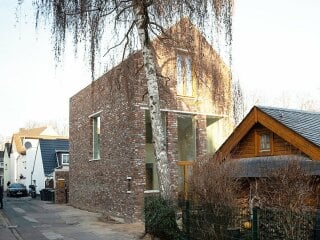 Für ein kleines Grundstück in einer schmalen Gasse mit heterogener und kleinteiliger Bebauung, entwarf der Kölner Architekt Till Robin Kurz ein Einfamilienhaus mit monolithisch wirkendem Ziegelkleid. 
