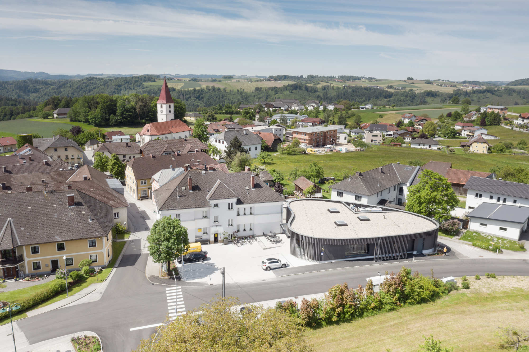 Die geschwungene Form des Neubaus und die umlaufende, dunkel lasierte Lärchenholzverschalung bilden einen Kontrast zur den benachbarten Gebäuden. 