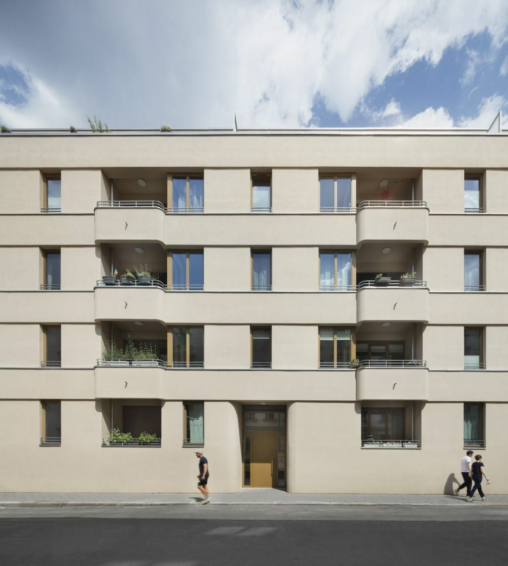 Der moderne, verputzte Ziegelbau reagiert auf die denkmalgeschützten Nachbargebäude aus der Gründerzeit, setzt jedoch eigene gestalterische Akzente: Abgerundete Ecken prägen die Eingänge.
