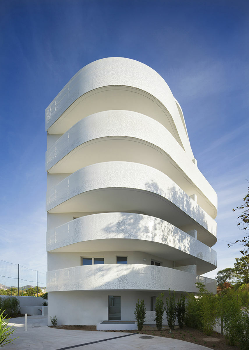 Nach Süden hingegen, wo sich eine kleine Grünfläche mit altem Baumbestand befindet, ist die Fassade sanft geschwungen mit abgerundeten Ecken und umlaufenden, laubengangartigen Balkonen.
