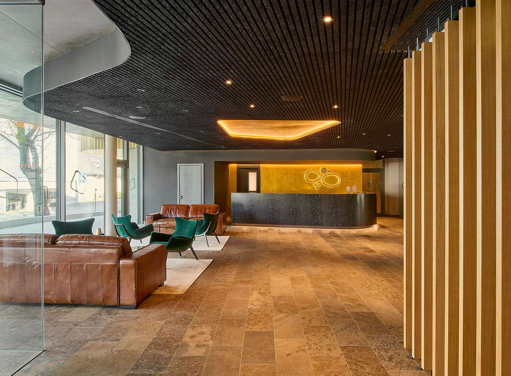 Von der Viktoriaallee aus gelangt man ins Foyer, in dem hochwertige, natürliche Materialien wie Naturstein, Holz und Leder für ein elegantes und zugleich warmes Ambiente sorgen.