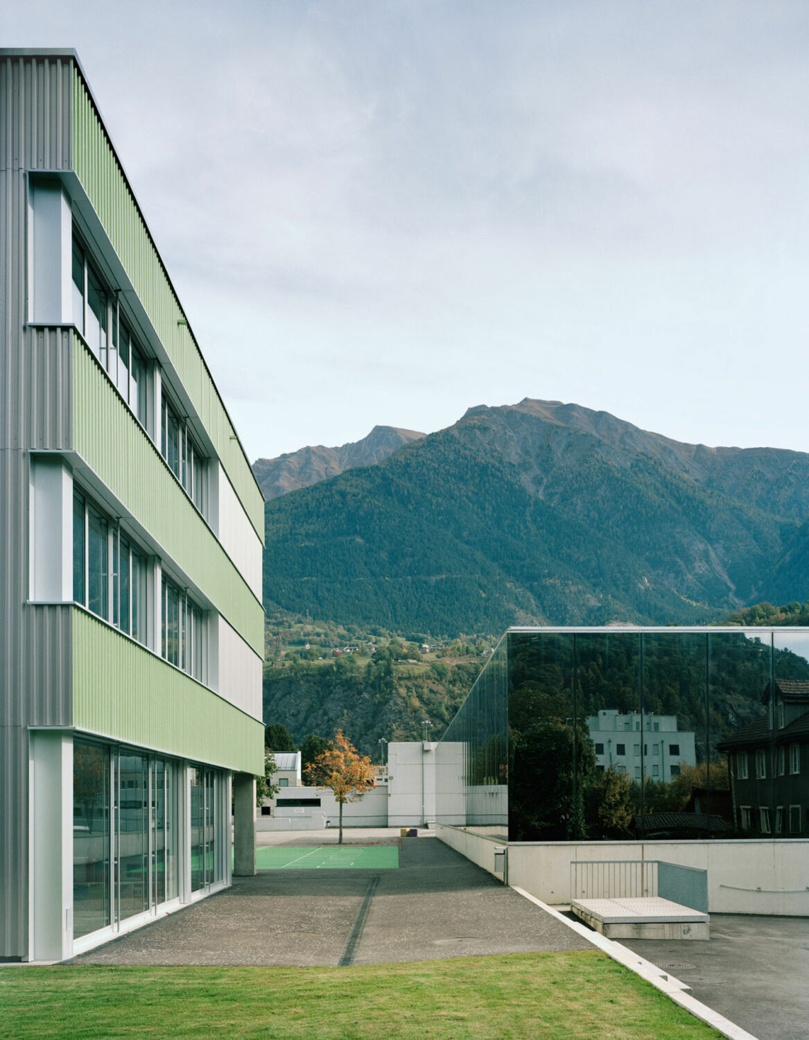 Horizontale Bahnen aus grünen Acryl-Wellplatten und großzügige Fensterbänder prägen die Fassade.