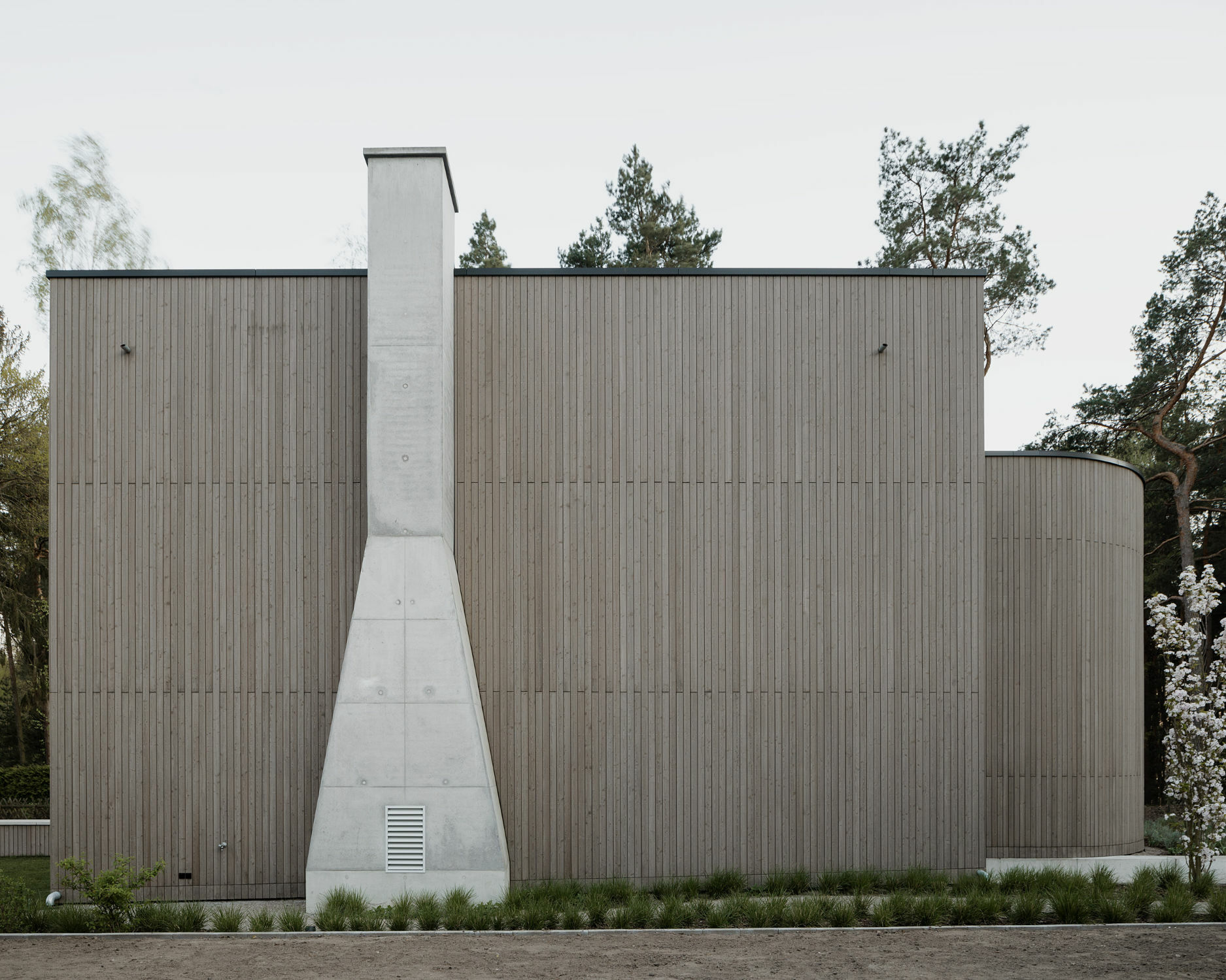 An der nördlichen Fassade hebt sich der Kamin aus Sichtbeton gegen die hölzerne Fassadenbekleidung ab.