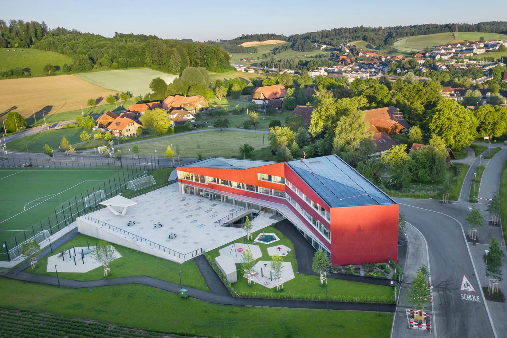 Der Pausenhof befindet sich auf einem Betonsockel, der dem nach Südwesten abfallenden Hang entwächst. Er beherbergt die Turnhalle sowie Umkleide-, Sanitär- und Geräteräume.