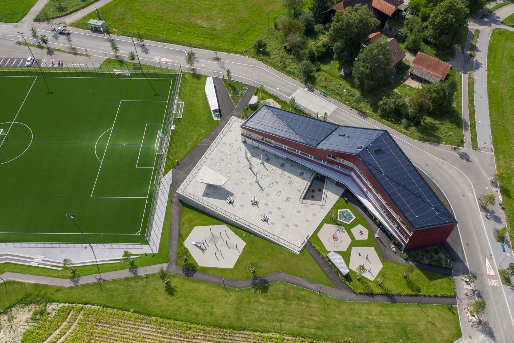 Der offene Winkel des Schulhauses nach Plänen von Büning-Pfaue Kartmann Architekten bildet den Übergang zwischen den entstehenden fünfgeschossigen Zeilenbauten und dem denkmalgeschützten Bauernweiler.