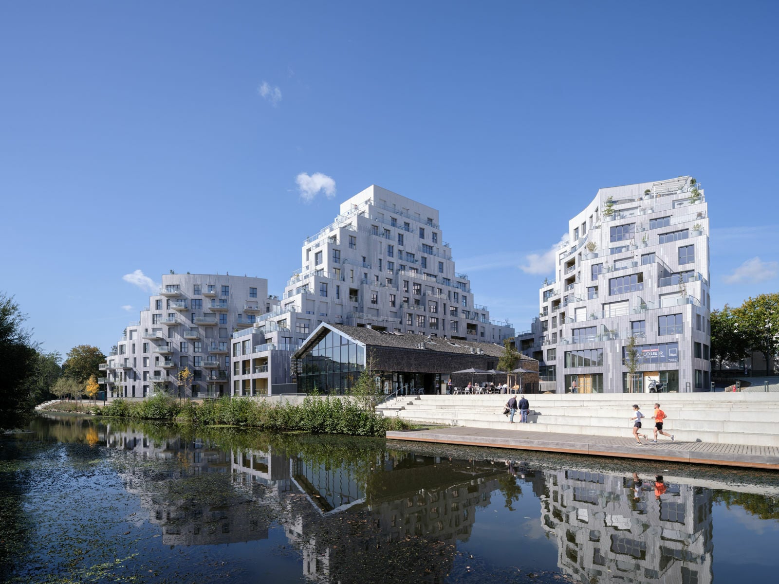 Im Erdgeschoss definieren die Kurven der beiden Gebäude u.a. eine begrünte Fußgängerzone und einen öffentlichen Platz am Wasser, der zu einem Restaurant und Theater führt.