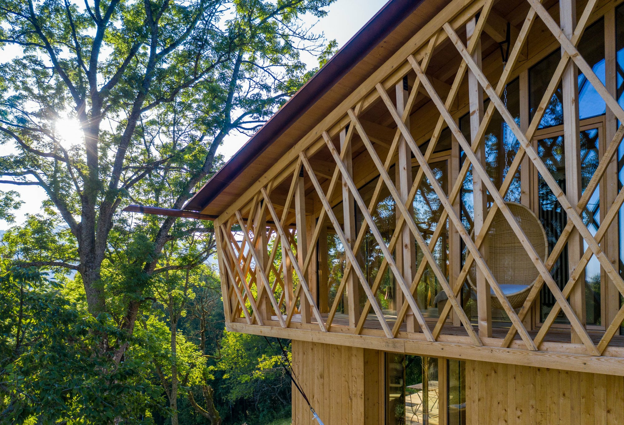 Ein Holzgeflecht umfasst das Obergeschoss und scheint sich mit den Ästen zu verwinden. 