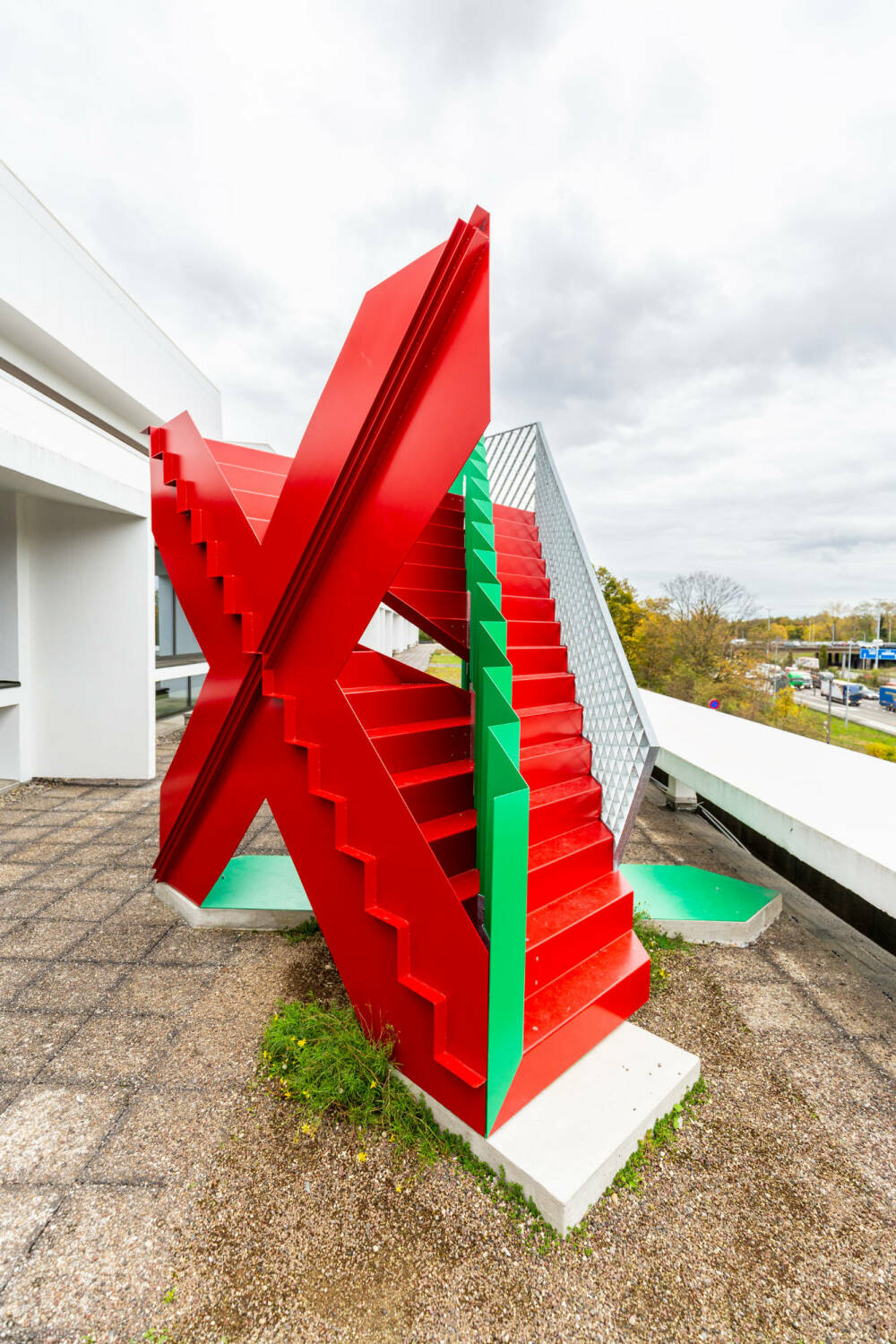 Die Skulptur besteht aus einer roten und einer grünen Treppe, die ineinander verschränkt sind.