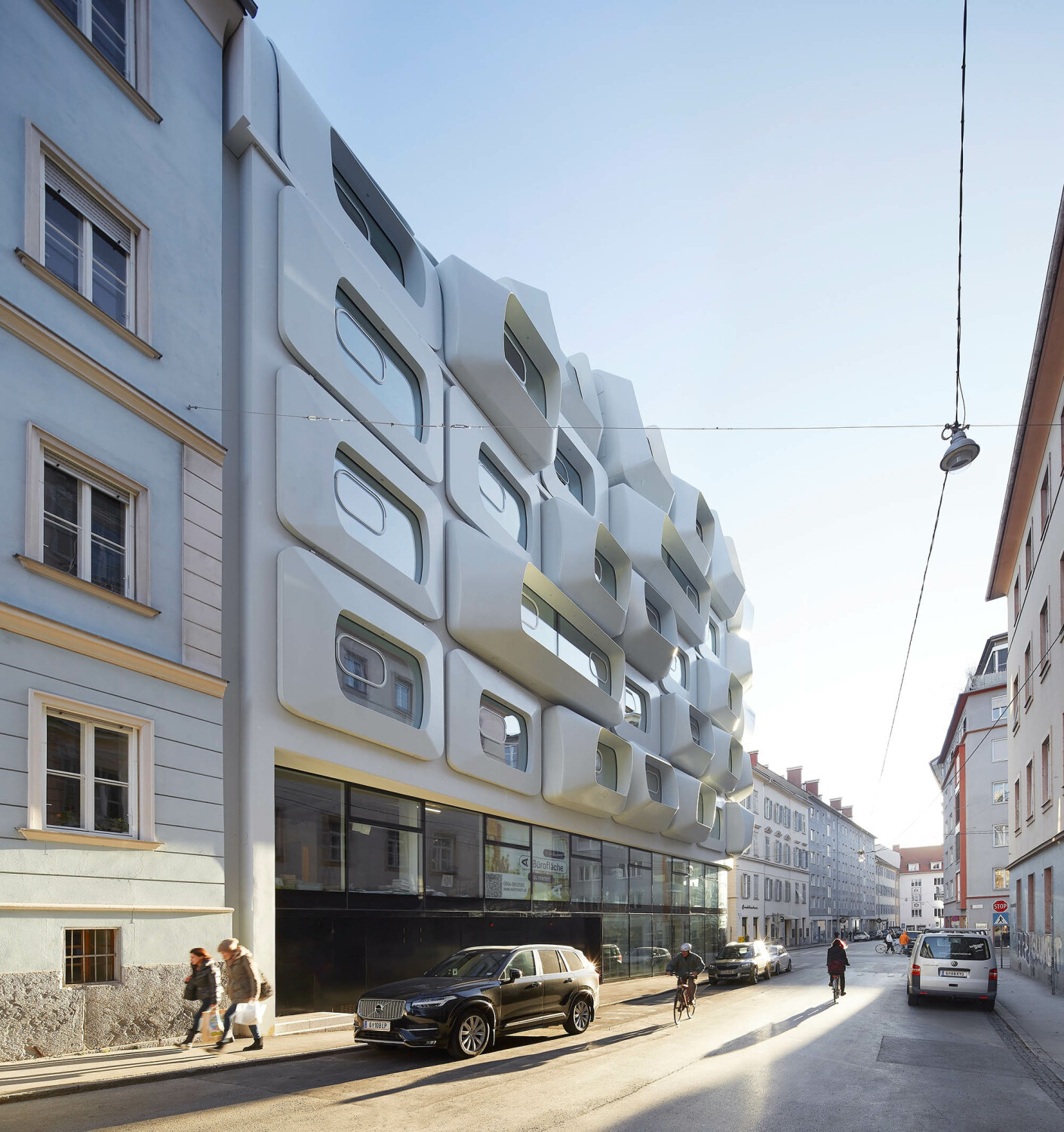Die Fassade ist zweigeteilt und besteht aus einer rückversetzten, gläsernen Sockelzone und der markanten Lochfassade in den oberen Geschossen. 