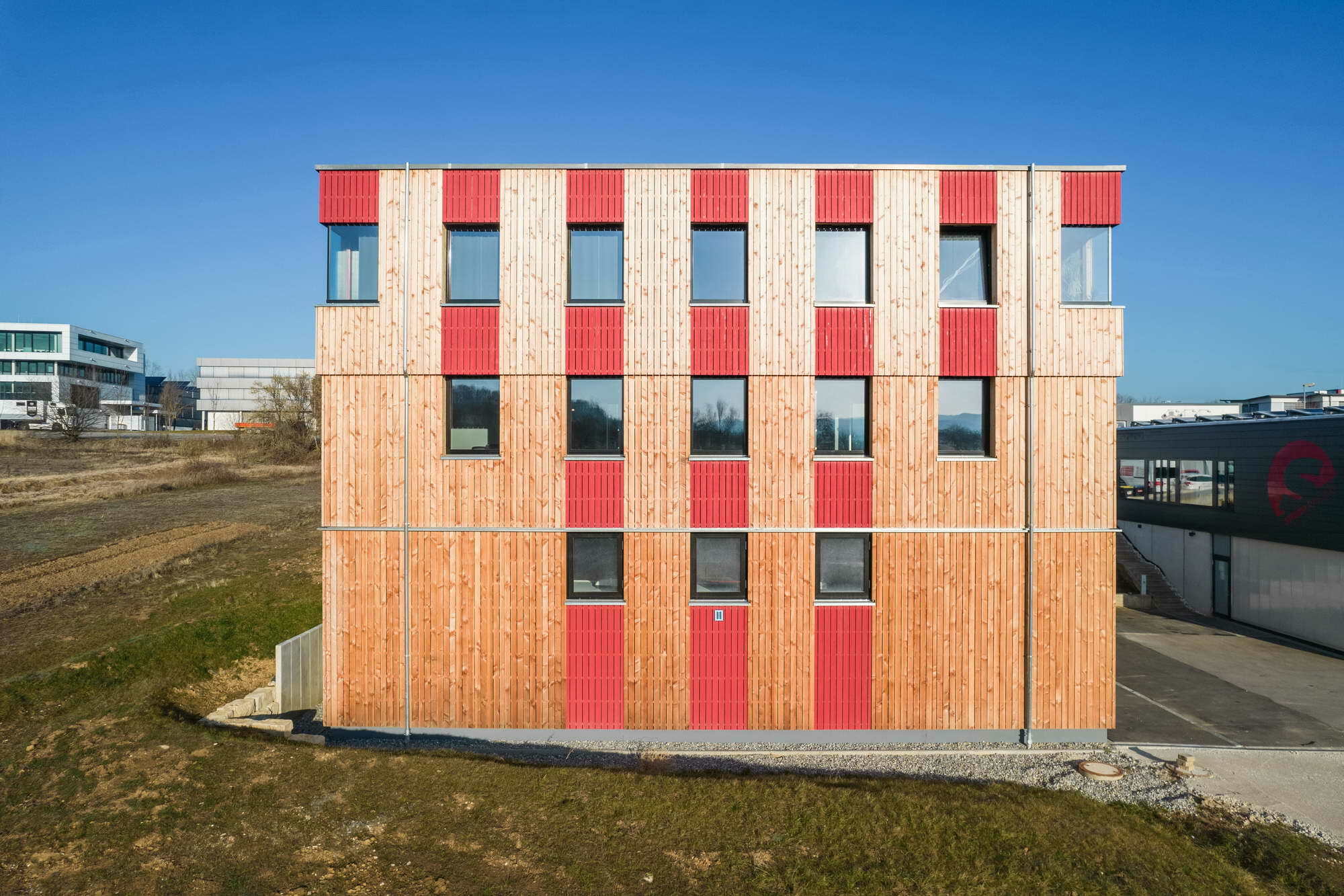 Der annähernd würfelförmige Baukörper mit Lärchenholzfassade und rot akzentuierten Fensterflächen bietet eine Nutzfläche von fast 900 Quadratmetern.