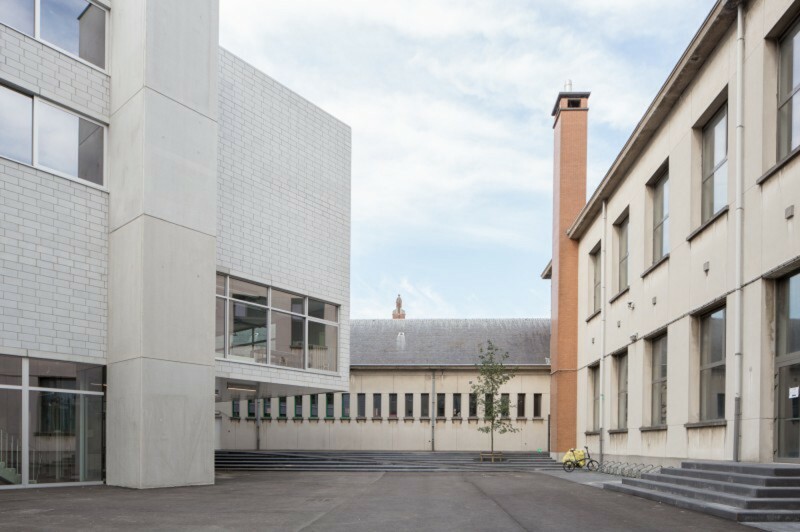 Das Brüssler Architekturbüro Agwa entwarf einen viergeschossigen Neubau, dessen Sockel zwar den rechteckigen Grundriss der bestehenden drei Riegel aufnimmt, die Obergeschosse jedoch wandeln sich zum Kubus und drehen in einem 53-Grad-Winkel vom Erdgeschoss ab. 