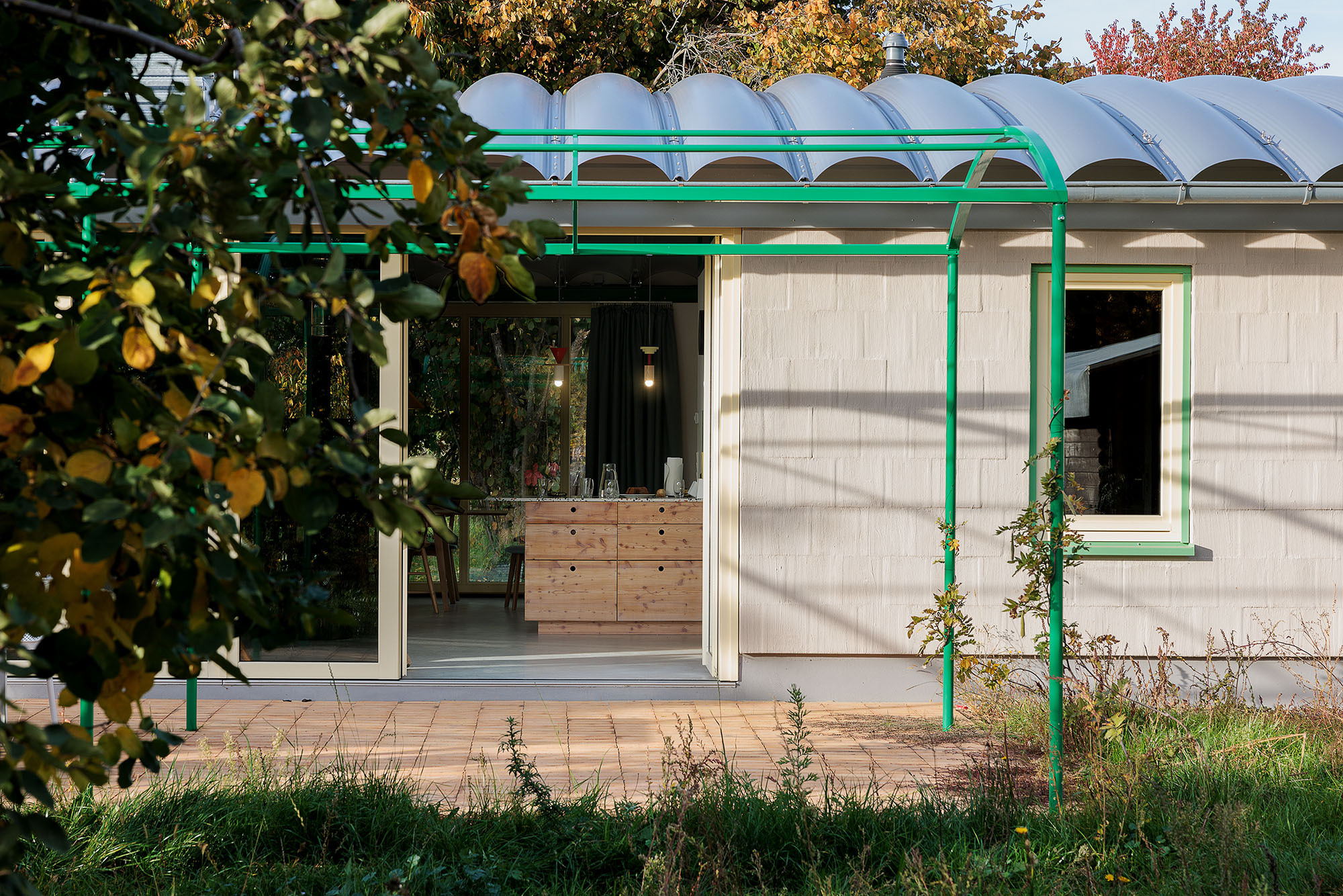 Industriebau-Elemente prägen die Architektur, etwa das Sandwich-Bogendach und die Pergola aus grünen Metallrohren.
