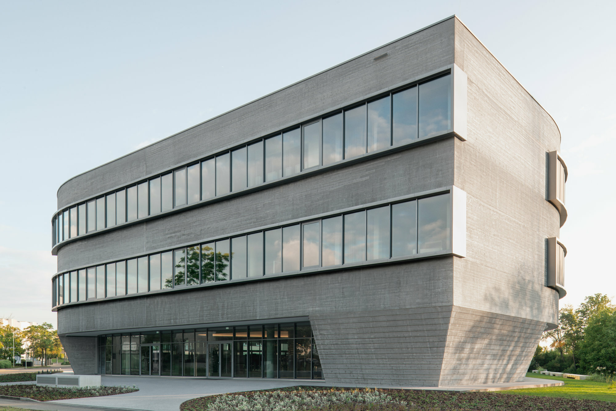 Lange Fensterbänder „knicken“ sich spielerisch um die Rundungen der Beton-Fassade.